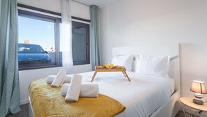 A hotel room with a bed, a window with curtains, a bedside table with a lamp, and a tray with breakfast items. - Aqui H Casa by Atlantic Holiday (Santa Cruz)