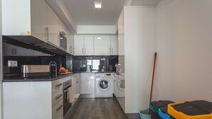 A compact kitchen with a washing machine, a coffee maker, and a broom. - Aqui H Casa by Atlantic Holiday (Santa Cruz)