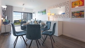 A modern dining area with a glass table, blue chairs, and a white cabinet. - Aqui H Casa by Atlantic Holiday (Santa Cruz)