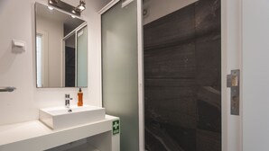 A bathroom with a white sink, a mirror, and a green emergency sign. - Aqui H Casa by Atlantic Holiday (Santa Cruz)