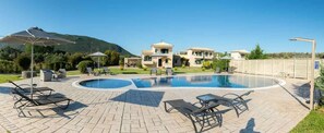 A pool area with lounge chairs, a circular pool, and a building with multiple balconies.