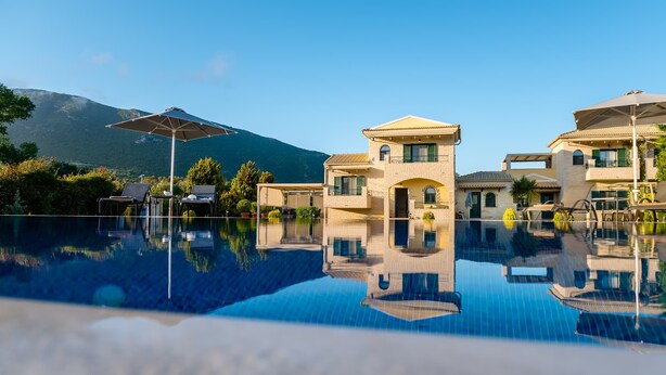 Une piscine dont l’eau est si claire qu’elle reflète parfaitement l’environnement, un bâtiment à deux étages doté d’un balcon, et une montagne en arrière-plan.