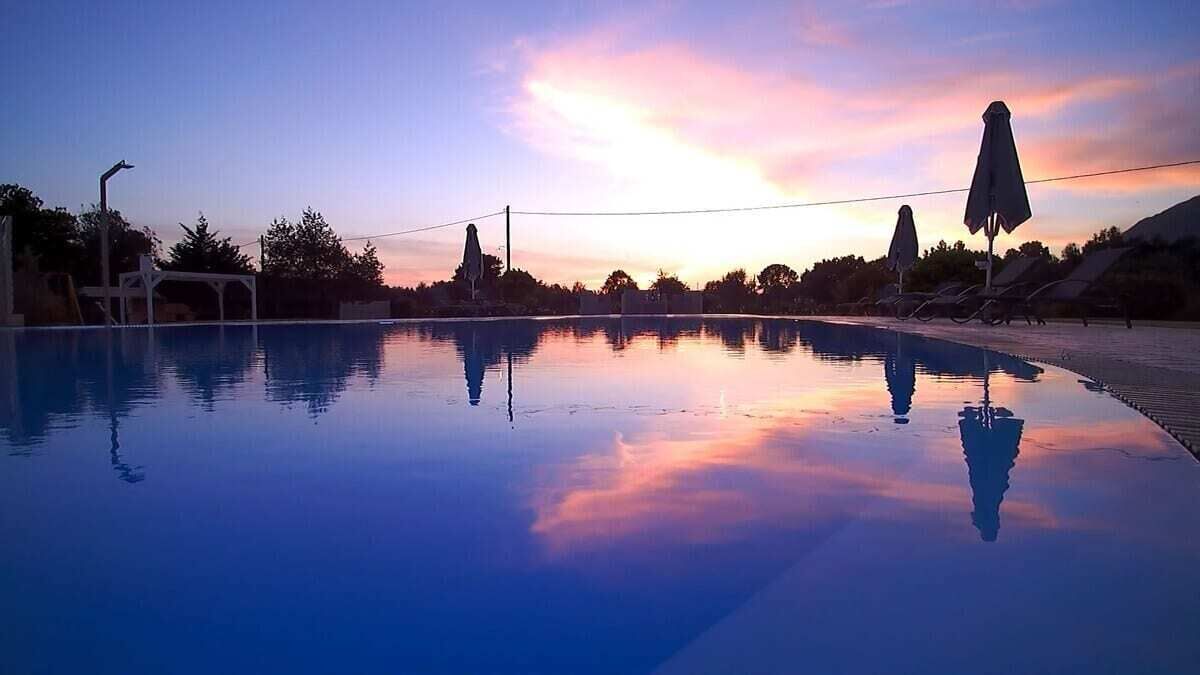 Une piscine à l’eau claire qui reflète le ciel au coucher du soleil, entourée de chaises longues et de parasols.
