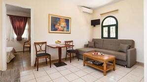 Un salon comprenant un canapé, une table basse et une table à manger avec des chaises. Un tableau est accroché au mur et un appareil de climatisation est fixé au mur.