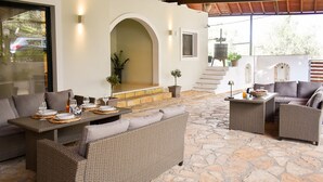 An outdoor patio with wicker furniture, stone flooring, and a view of the street. - Casa Ankilena Corfu Garden Haven (Corfu)
