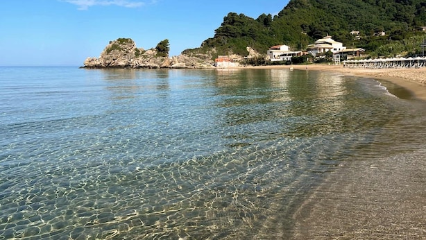 A coastal beach with clear waters, rocky outcrops, and buildings on a hillside. - Casa Ankilena Corfu Garden Haven (Corfu)