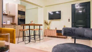 A modern living room with a sofa, a dining table, and a TV mounted on the wall. - Casa Ankilena Corfu Garden Haven (Corfu)
