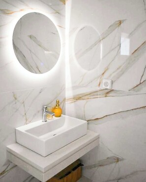 A bathroom with a white sink, a round mirror, and a marble-patterned wall.