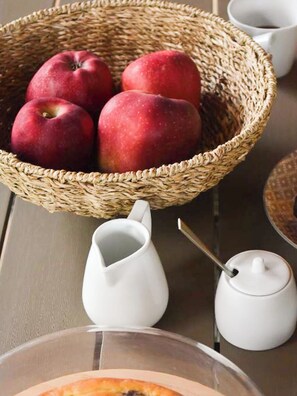 A wicker basket with red apples, a white pitcher, and a small white container on a table.