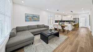 Een moderne woonkamer met een grijze hoekbank, een salontafel en een eethoek met een houten tafel en stoelen.