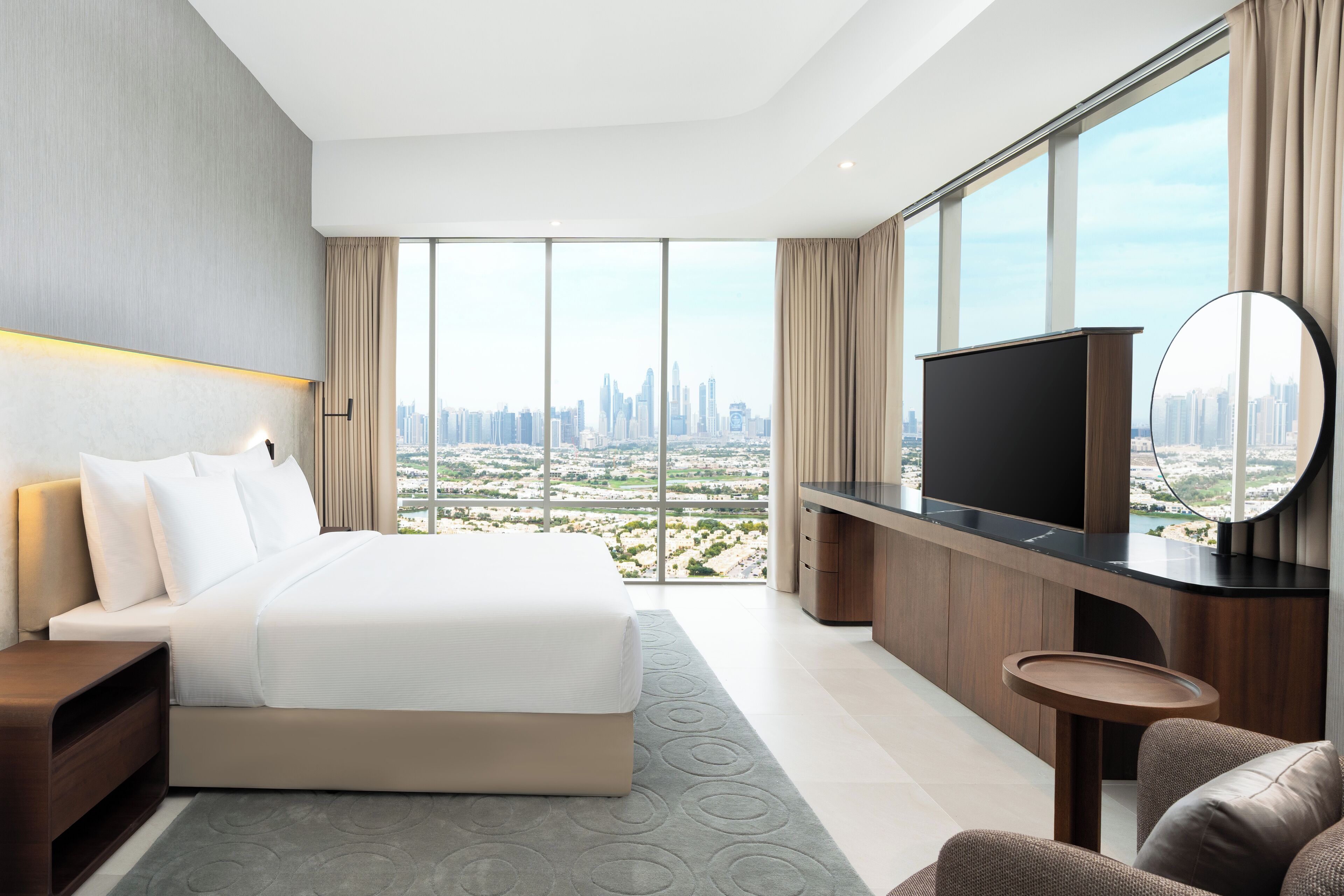 Une chambre d’hôtel moderne dotée d’un grand lit, d’une télévision, d’un bureau et offrant une vue sur le paysage urbain.
