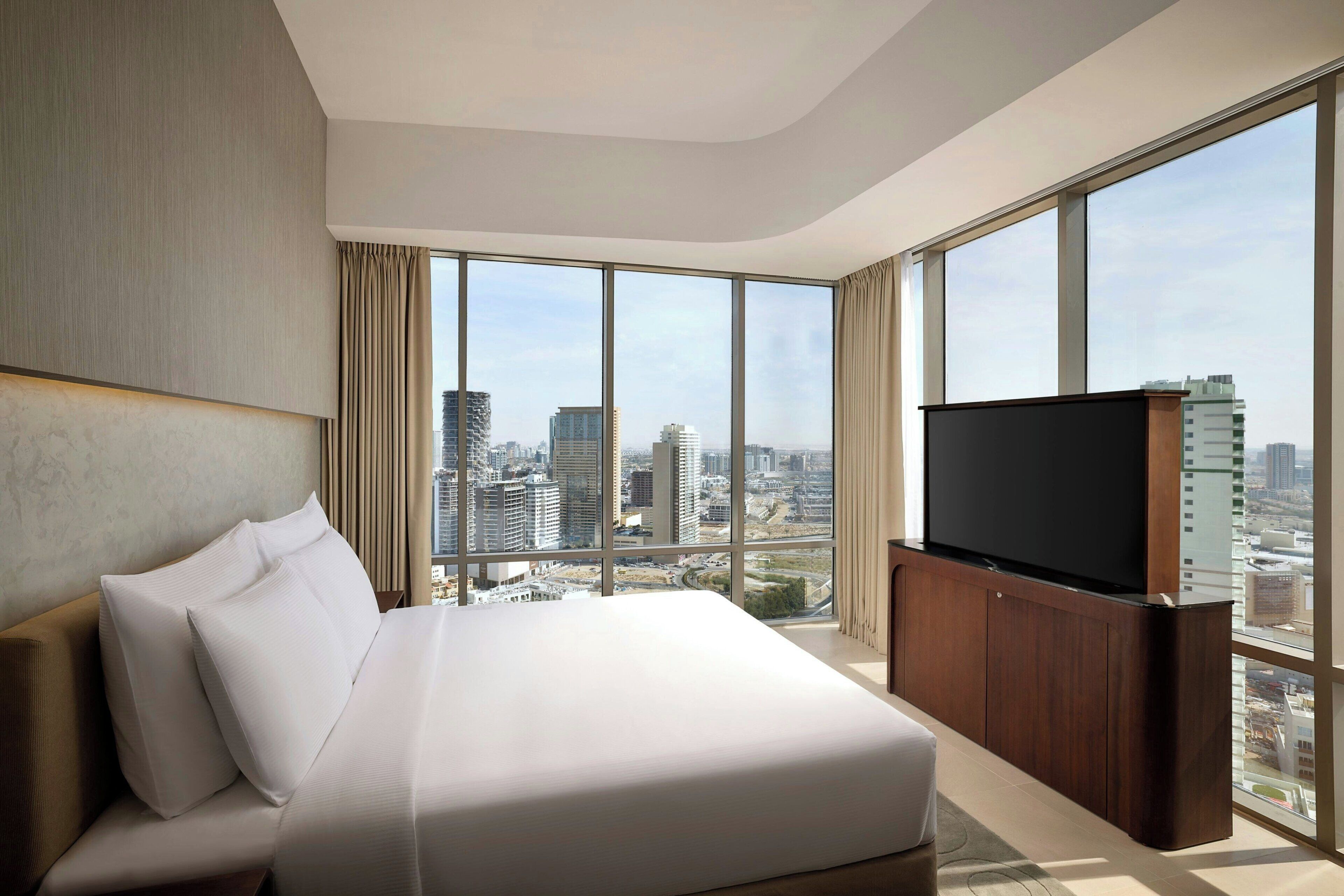 Une chambre d’hôtel moderne dotée d’un grand lit, d’un téléviseur à écran plat et offrant une vue sur la ville grâce à de grandes fenêtres.