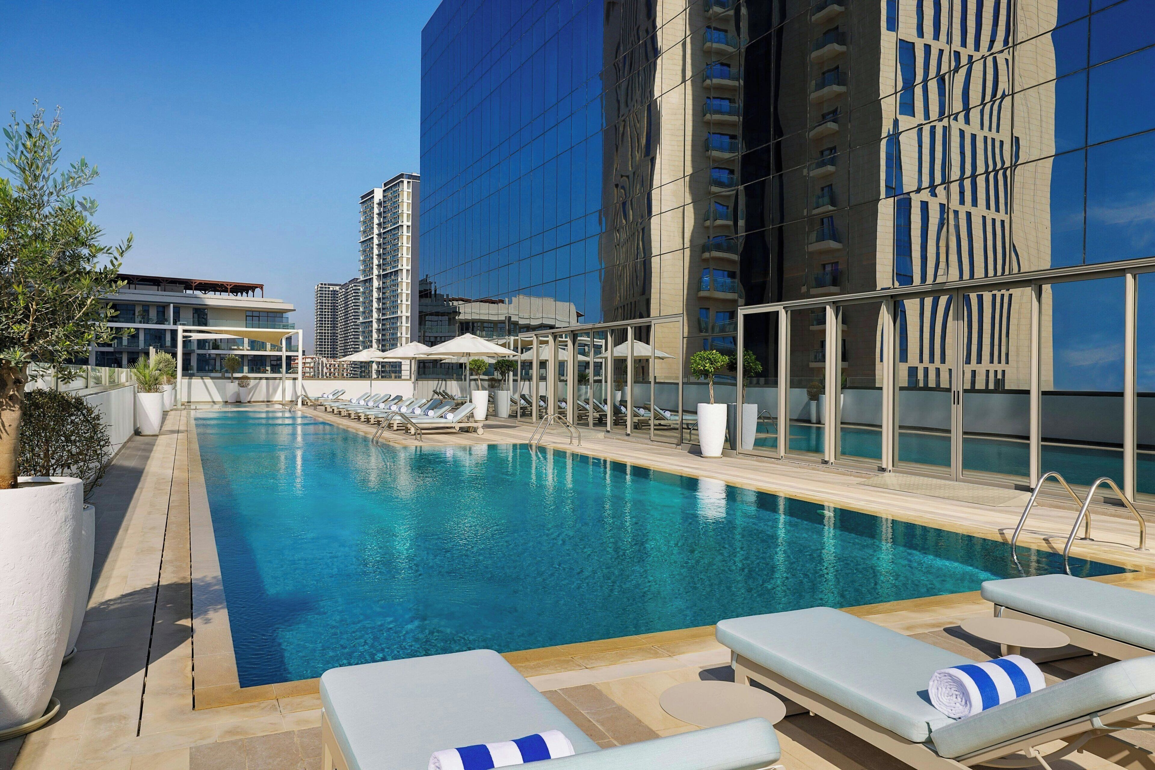 A rooftop pool with lounge chairs and umbrellas, surrounded by modern buildings.