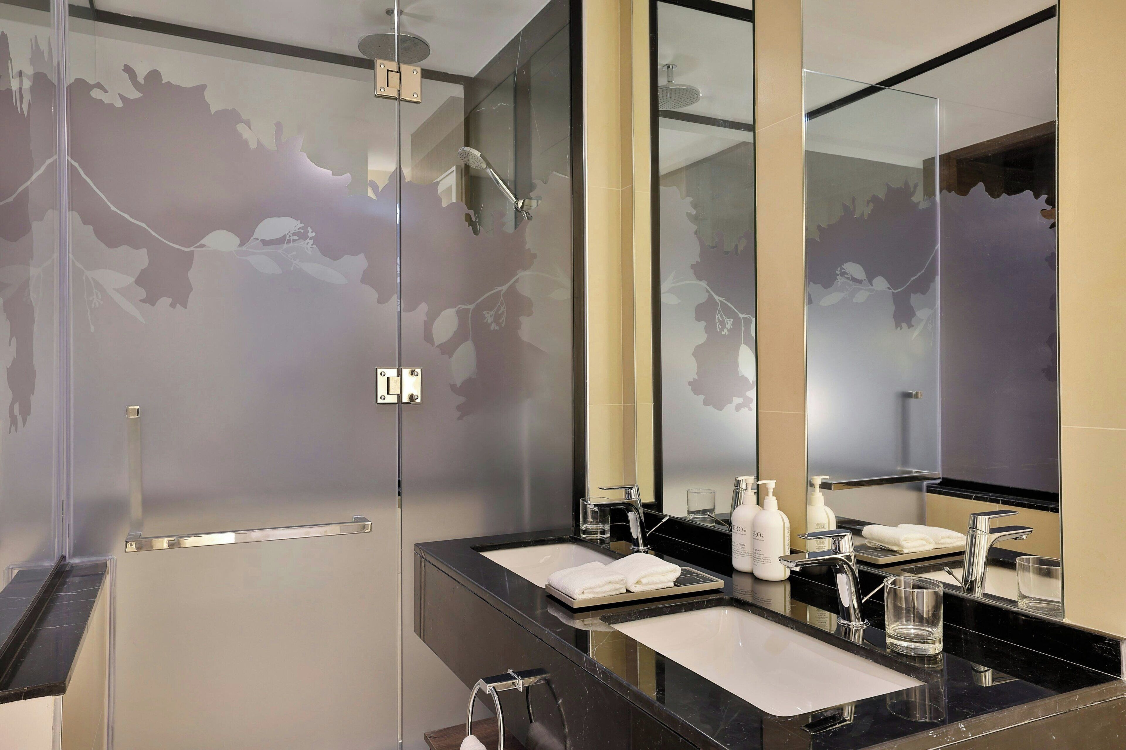 A modern bathroom with a glass-enclosed shower, dual sinks, and a large mirror.