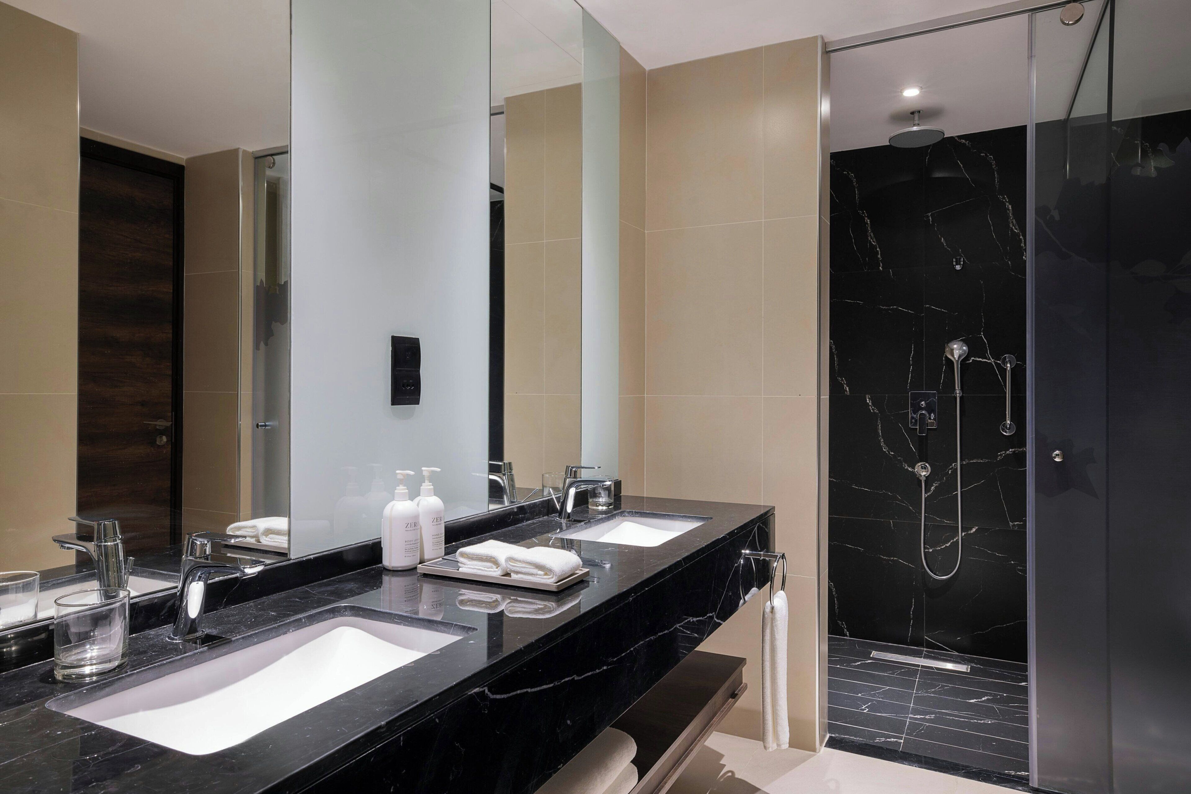 A modern bathroom with two sinks, a large mirror, and a glass-enclosed shower area.