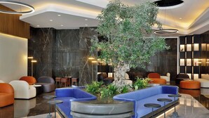 A modern lobby with a central seating area, a large tree, and a marble floor. - Hotel Local Dubai, Jumeirah Village Triangle, Autograph Collection (Dubai)