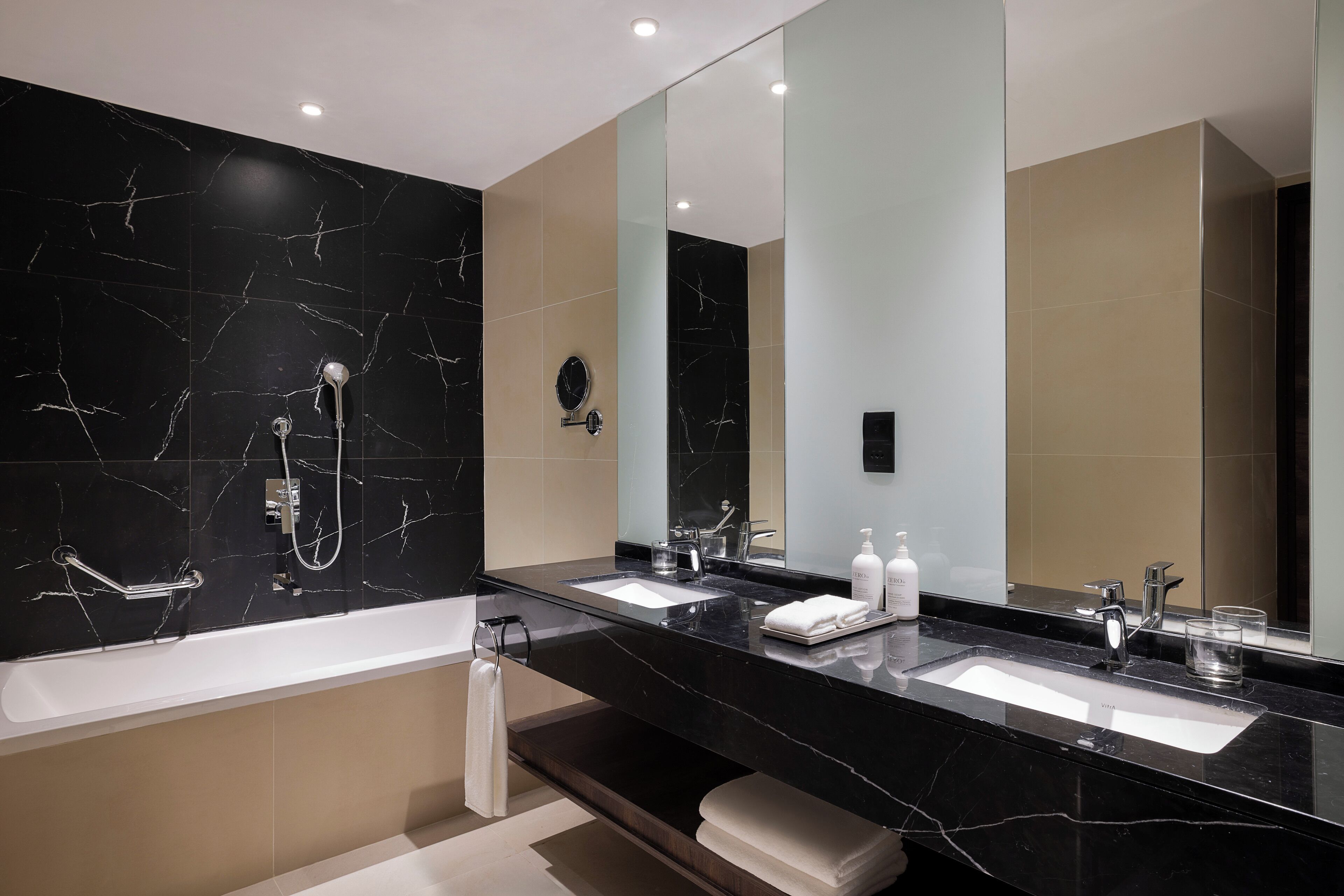 A modern bathroom with a black marble vanity, two sinks, a bathtub, and a large mirror.