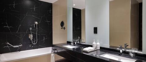 A modern bathroom with a black marble vanity, two sinks, a bathtub, and a large mirror.