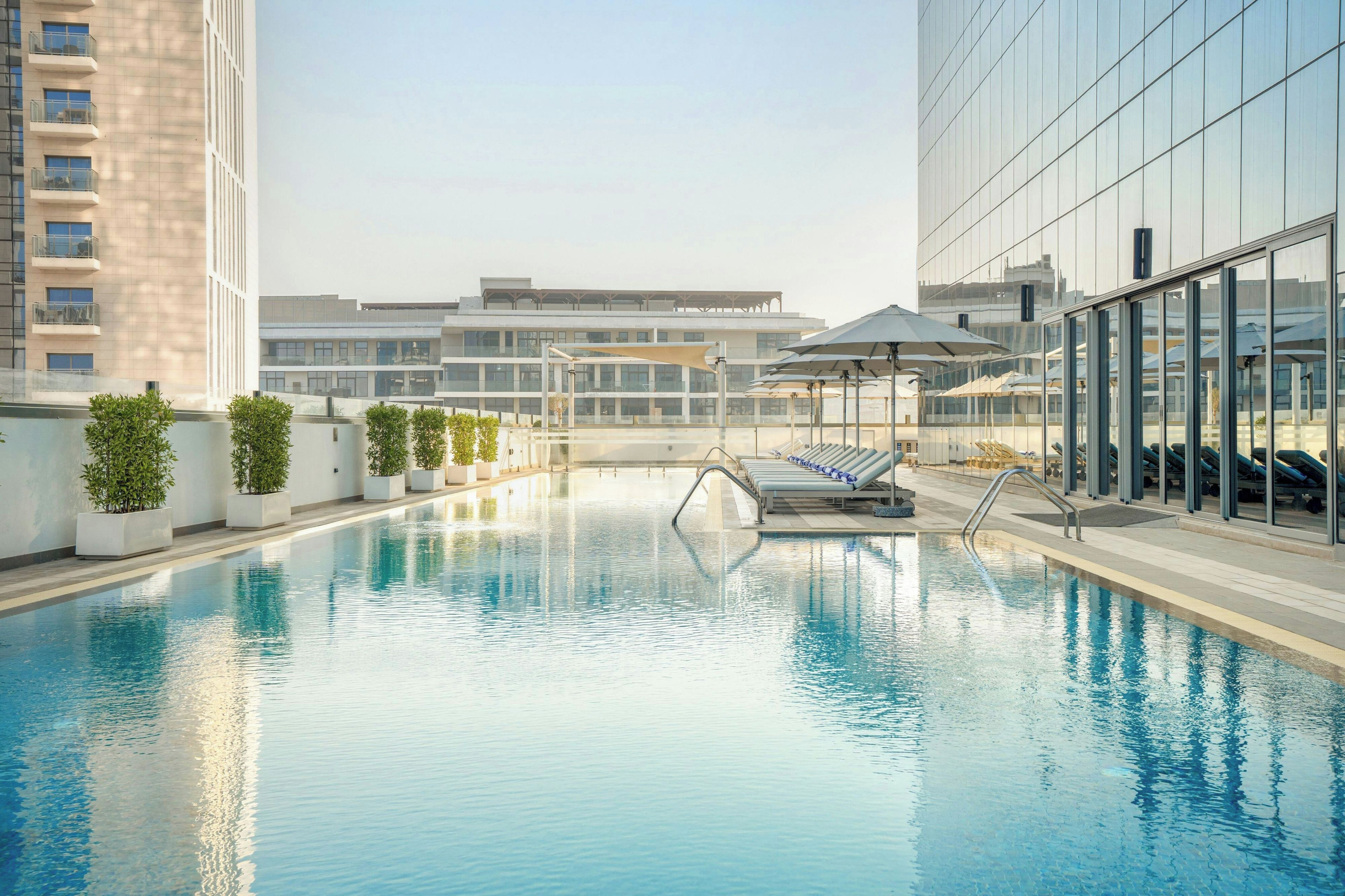 Une piscine sur le toit, agrémentée de chaises longues et de parasols, et entourée d’immeubles modernes.
