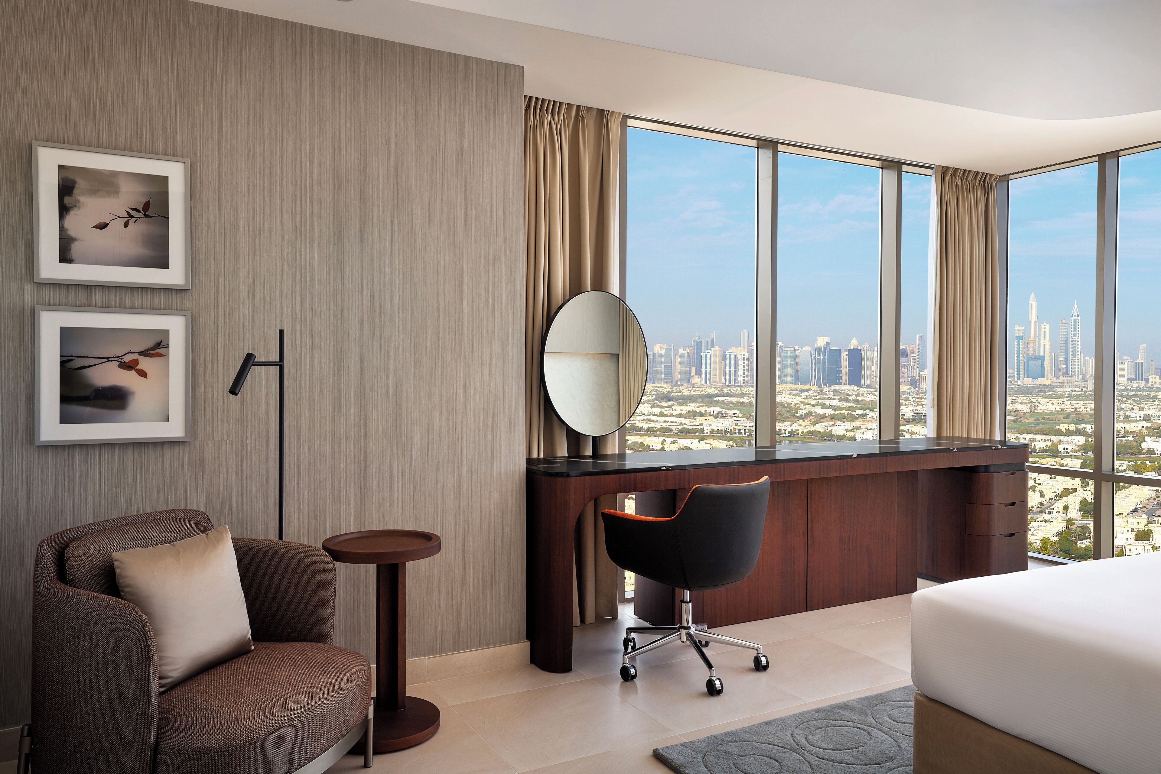 A modern hotel room with a large window offering a city view, a comfortable sofa, a desk with a chair, and a bed.