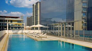 A rooftop swimming pool with sun loungers and umbrellas, surrounded by modern buildings.