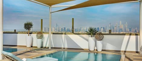 A rooftop pool area with lounge chairs, potted plants, and a city skyline view.