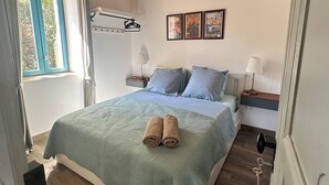 A bedroom with a wooden ceiling, a bed with a green bedspread, two pillows, a bedside table with a lamp, and a window with curtains. - Beautifully restored wine grower’s house with pool in stunning riverside village (Roquebrun)