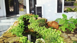 A garden area with various plants and rocks, a black door with decorative ironwork, and a white wall with a window. - Luxury home with Pool, Electric Vehicle charger in McAllen near by hospitals and (McAllen)