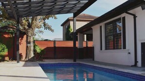 A swimming pool with a tiled deck, a wooden pergola, and a brick wall in the background. - Luxury home with Pool, Electric Vehicle charger in McAllen near by hospitals and (McAllen)