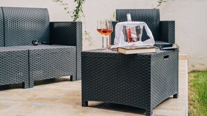 A wicker outdoor seating area with a table, a wine glass, and a bottle.