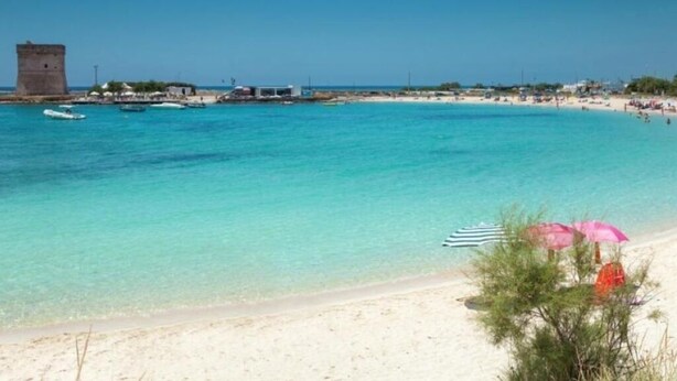 A beach with clear turquoise water, a sandy shore, and a few umbrellas.