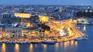 A coastal cityscape with a marina, buildings, and a waterfront promenade.