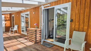 A modern room with wooden walls, a glass door leading outside, a white chair, and a small table with a vase.