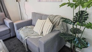 A living room with a grey sofa, striped pillows, a patterned throw, and a large green plant.