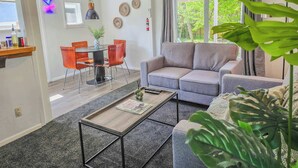 A modern living room with a grey sofa, a coffee table, and a dining area with orange chairs.