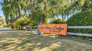 A wooden sign with the text 'Lake Tekapo Lodge by Ohana' in a natural setting with trees and a fence.