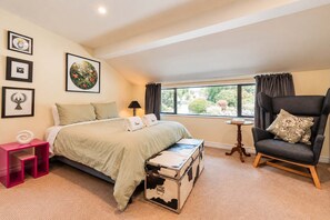 Un dormitorio con cama, una silla, una mesita y una ventana con cortinas.