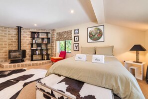 Een slaapkamer met een bed, een rode fauteuil, een boekenkast, een open haard en een ingelijst kunstwerk aan de muur.