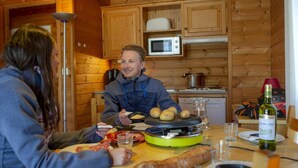 Ein Holzblockhaus-Interieur mit Esstisch, einem Transportkocher und einer Weinflasche.