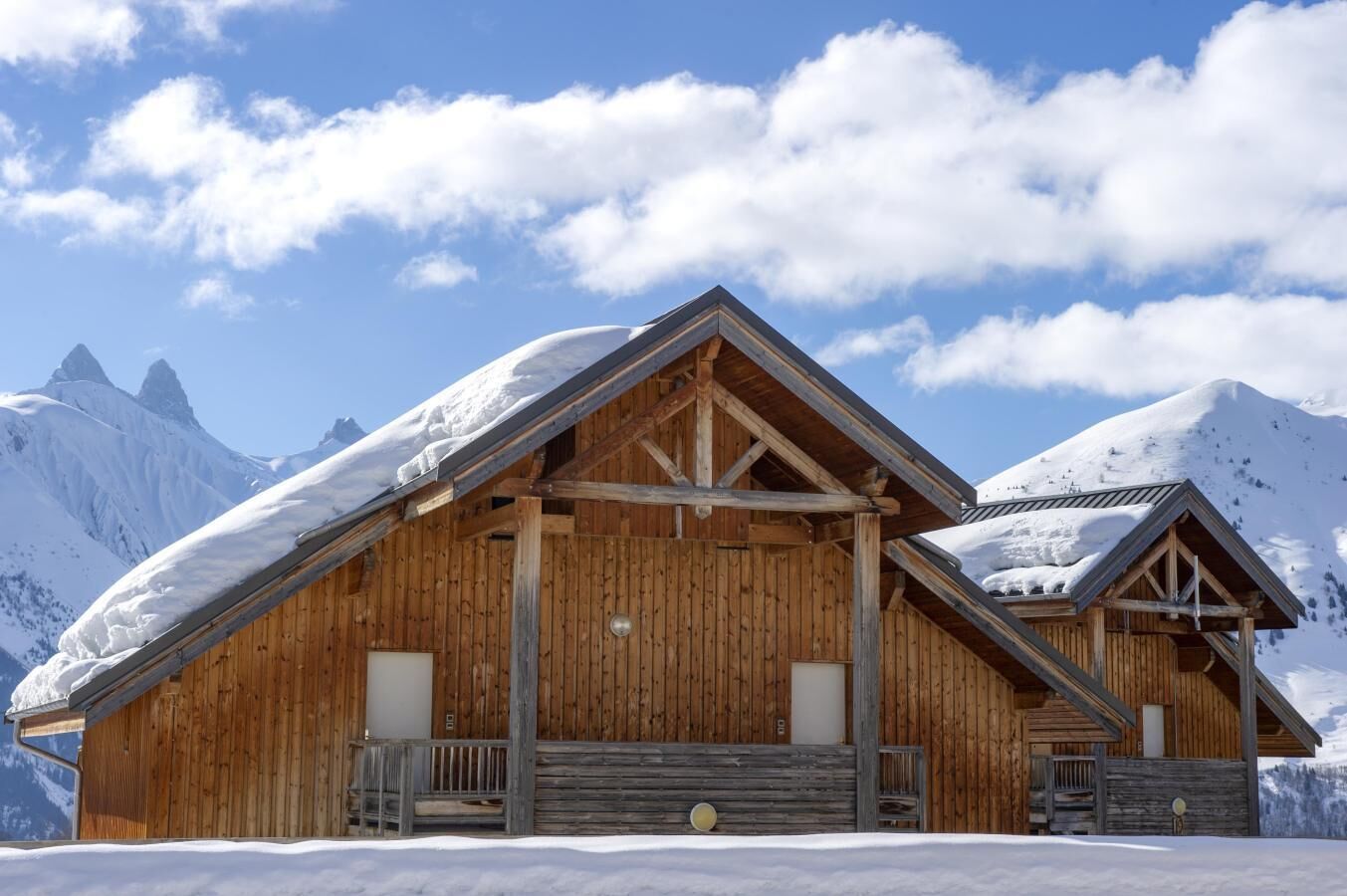 Een houten chalet met schuin dak, grote ramen en een balkon.