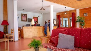 Et hotellobby med reception, træmøbler, en rød sofa med mønster og en plante på et bord.