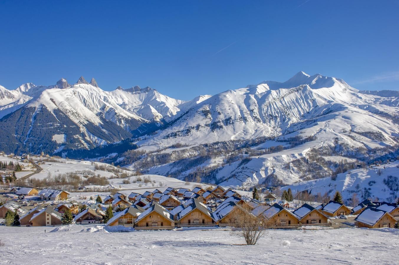 A snow-covered mountain village with wooden chalets and a clear view of the surrounding peaks.