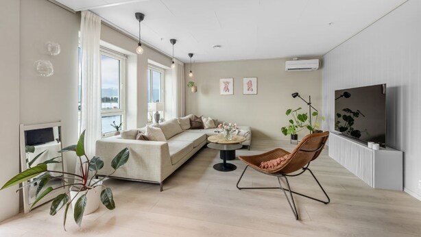 Una sala de estar moderna con un sofá, una mesa de centro redonda y un televisor. Hay plantas y una ventana con cortinas.