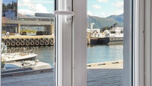 Vista desde el interior de un edificio hacia un muelle con barcos, una cubierta de madera y un paisaje montañoso al fondo.
