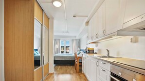 Una cocina moderna con armarios blancos, horno empotrado y ventana con vista a un dormitorio.