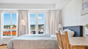 Una habitación de hotel con una cama, una mesa de madera y vistas al exterior a través de amplios ventanales.