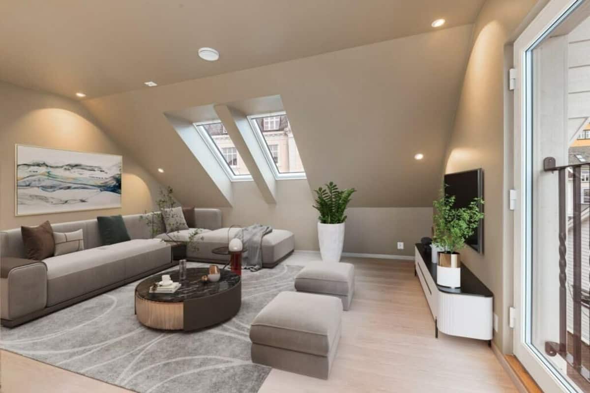 A modern loft-style living room with a sectional sofa, a round coffee table, and a large window with skylights.