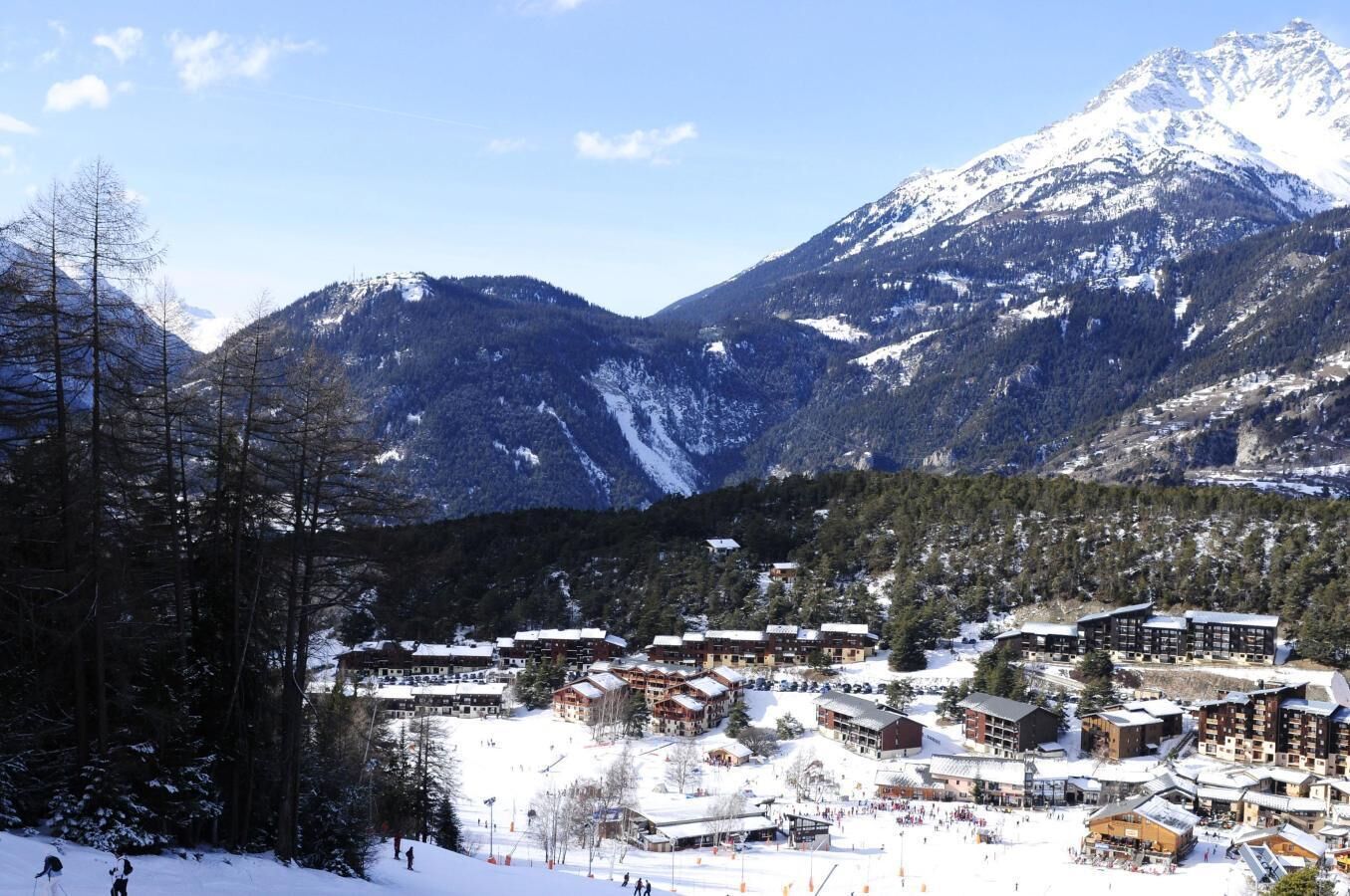 A snow-covered mountain town with multiple buildings, including a large lodge with multiple floors and a ski slope in the foreground.