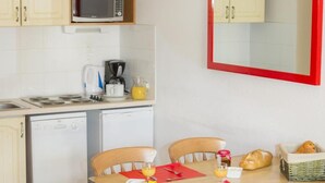 A compact kitchen with a microwave, coffee maker, and toaster on the countertop. There is a dining table with chairs, a small table with a candle, and a basket of bread. - Ski-in/ski-out & foot of the slopes, swimming pool, balcony, tv, ski locker, 50m², La Norma (La Norma)