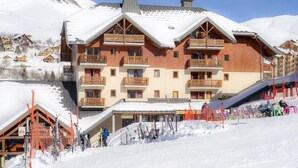 Un hôtel à plusieurs étages doté de balcons, proposant du matériel de ski et offrant une vue sur un paysage montagneux enneigé.